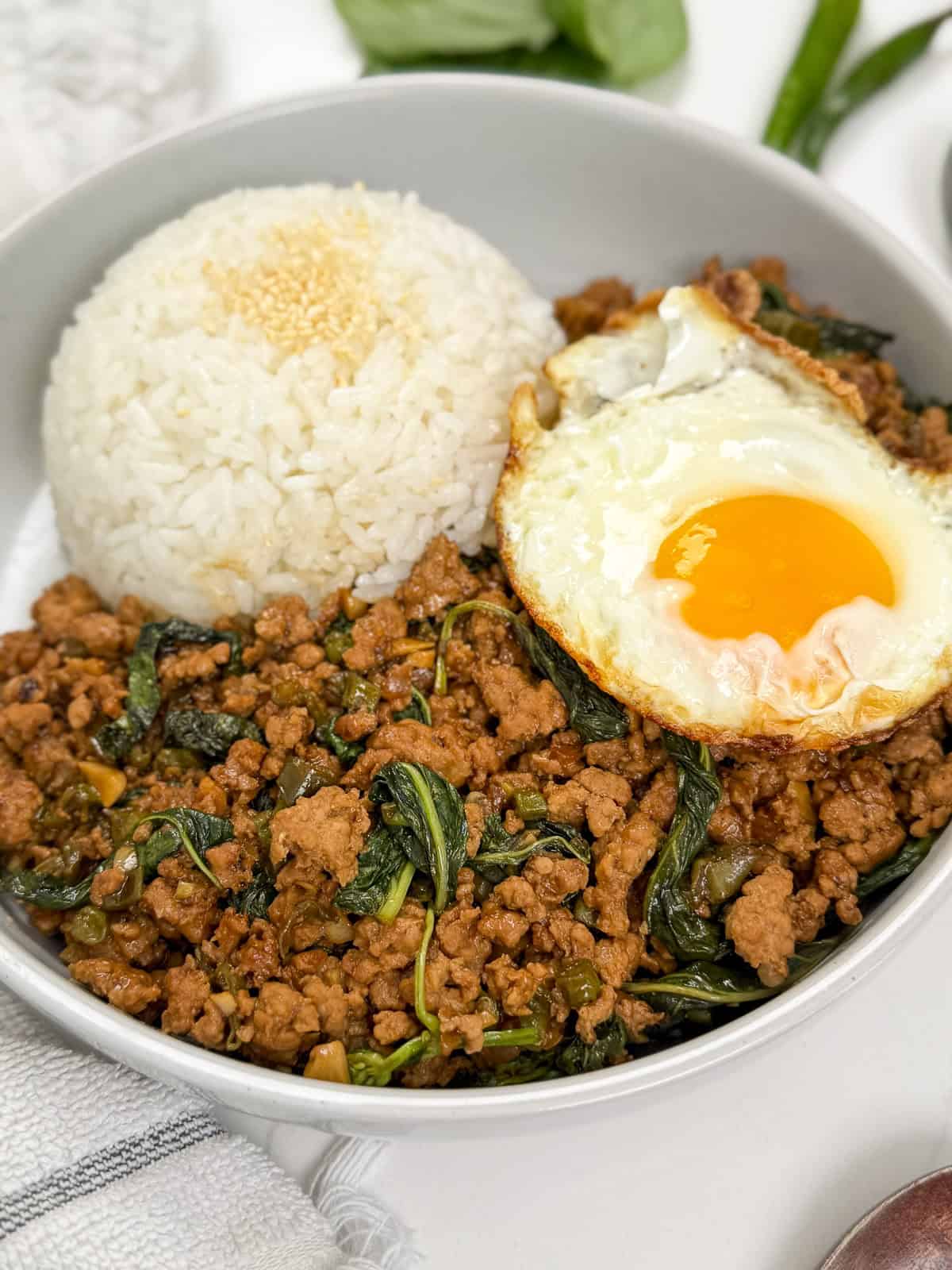 Pad Kra Pao (Ground Pork & Holy Basil Stir-Fry) in a bowl with white rice and fried egg side view
