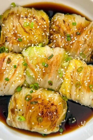 Napa cabbage rolls stuffed with chicken and veggies in sweet soy sauce and topped with sesame seeds, green onions, and chili oil featured view