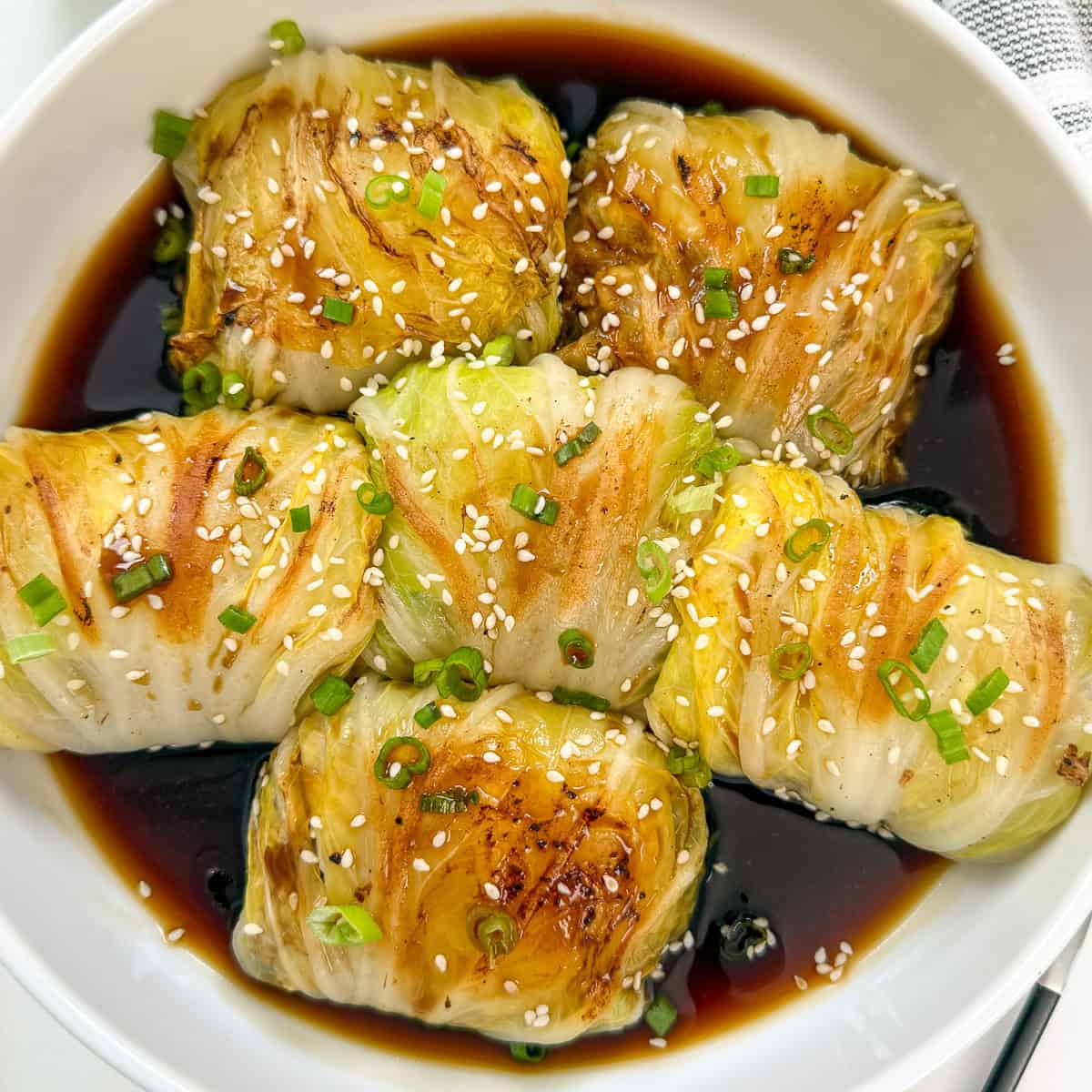 Napa cabbage rolls stuffed with chicken and veggies in sweet soy sauce and topped with sesame seeds, green onions, and chili oil featured view