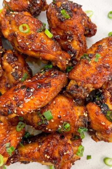 A plate of Honey Chili Oil Chicken Wings glazed to perfection, garnished with chopped green onions and sesame seeds, served on a white dish.