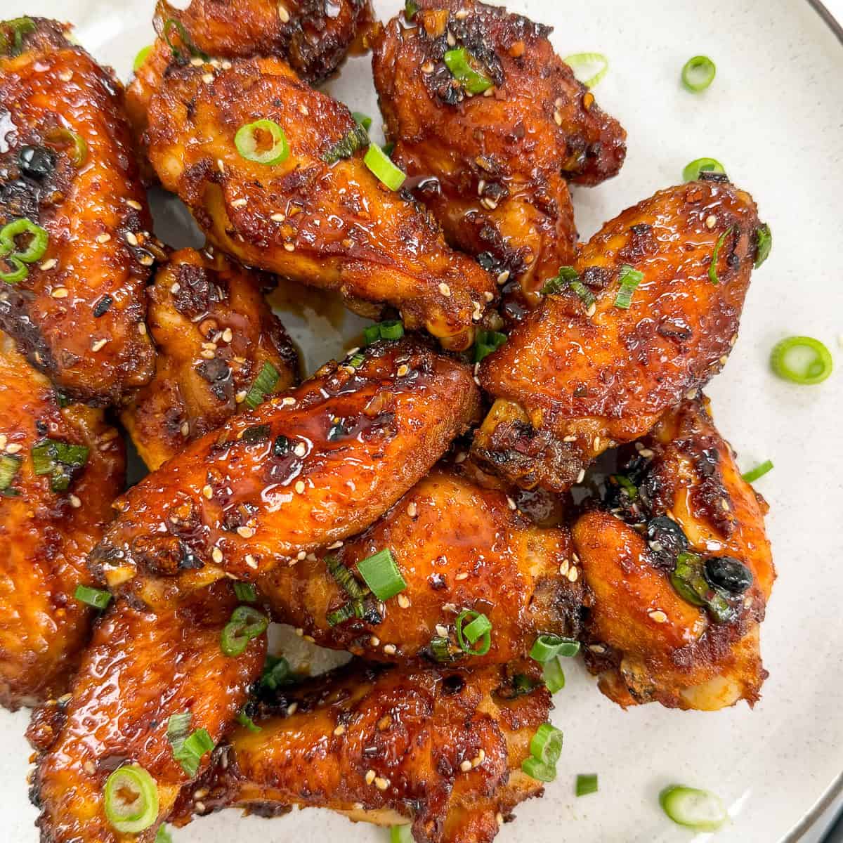 A plate of Honey Chili Oil Chicken Wings glazed to perfection, garnished with chopped green onions and sesame seeds, served on a white dish.