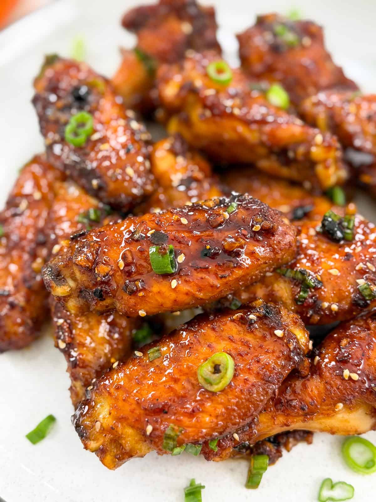 A close-up of crispy Honey Chili Oil Chicken Wings, glazed and garnished with sliced green onions and sesame seeds, served on a white plate.
