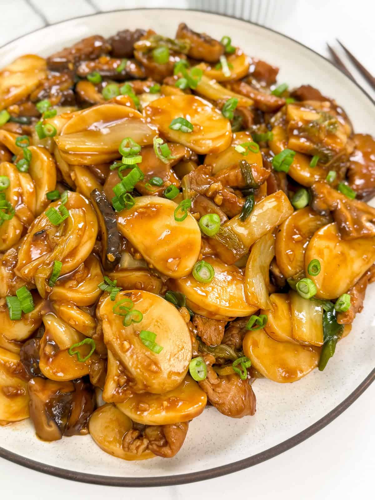 A plate of Shanghai rice cakes stir-fried with sliced beef, mushrooms, onions, and green onions, all coated in a glossy brown sauce. The dish is garnished with chopped green onions.