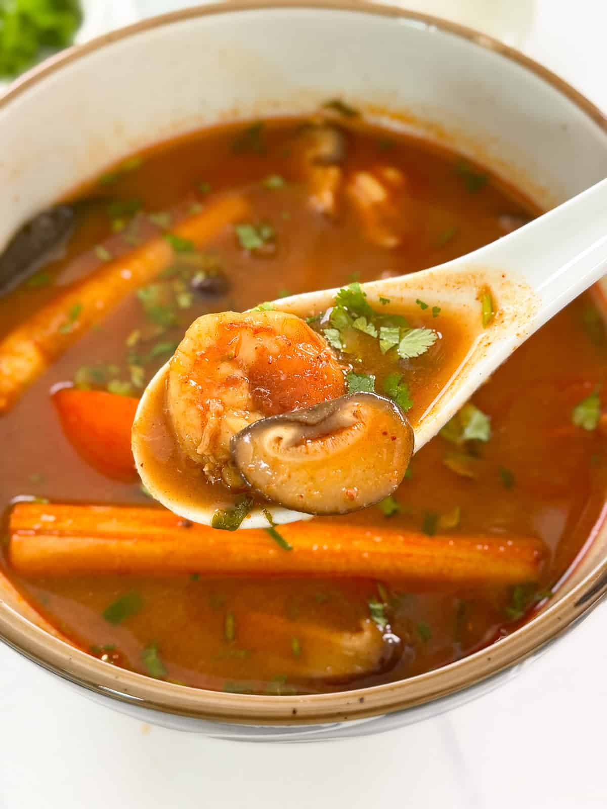 Bowl of Tom Yum Soup Recipe with a spoon of mushrooms and shrimp centered