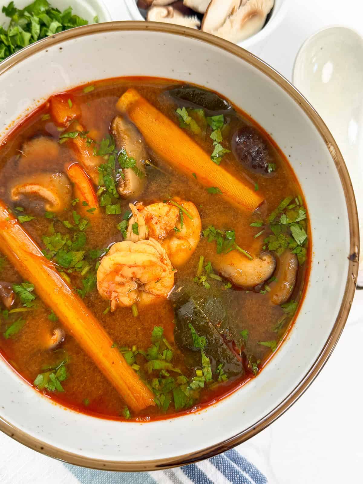 Bowl of Tom Yum Soup Recipe top down view with shrimp, lemongrass grass, kaffir lime leaves, and cilantro