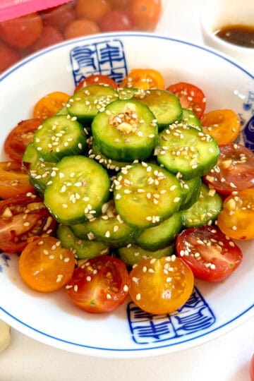 Asian Cucumber and Tomato Salad on a blue plate with cherry tomatoes scattered around