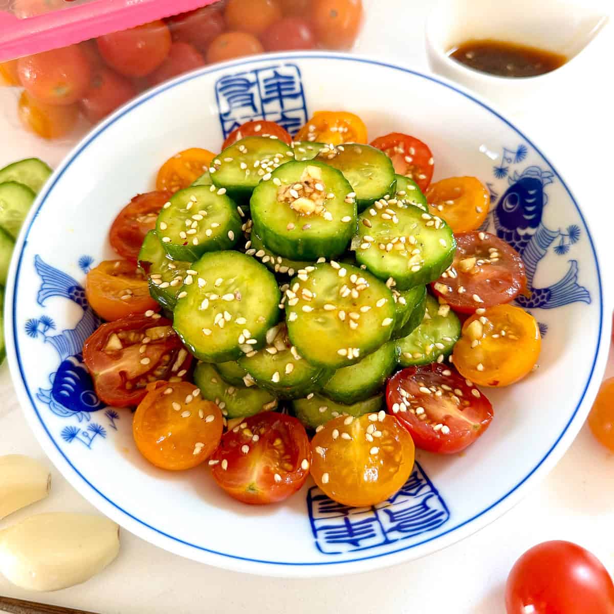 Asian Cucumber and Tomato Salad on a blue plate with cherry tomatoes scattered around