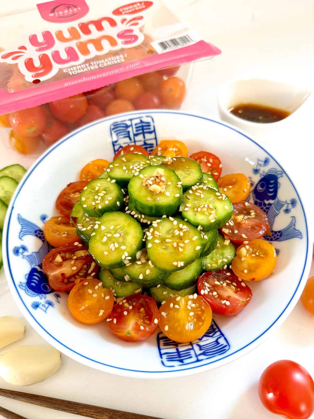 Asian Cucumber and Tomato Salad on a blue plate with chopsticks next to it and cherry tomatoes scattered all over.