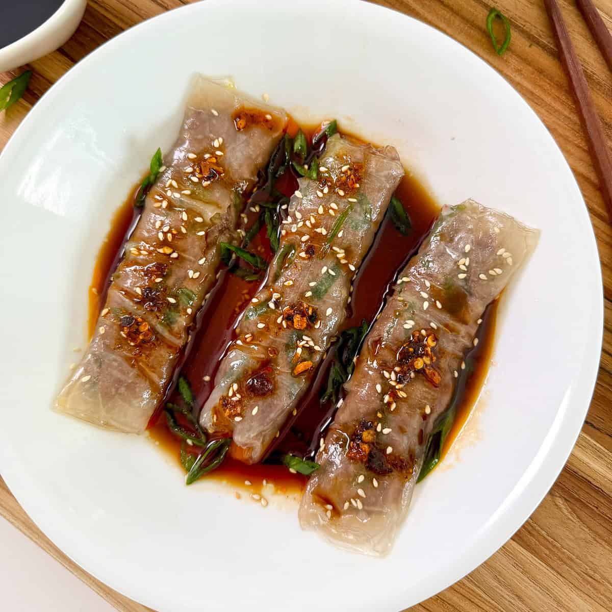 Beef Rice Paper Noodle Rolls (Cheung Fun) on a white plate with soy sauce and sesame seeds
