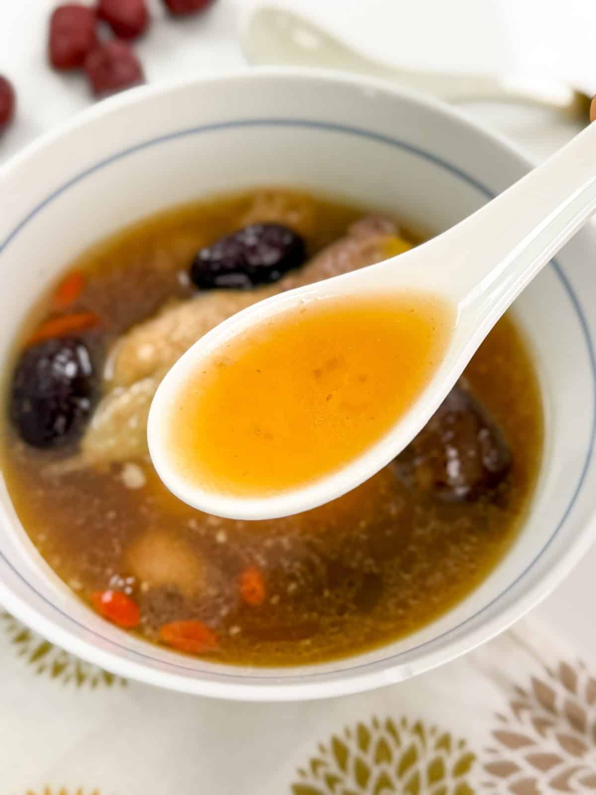 Chinese Chicken Herbal Soup with a white spoon holding the soup in the middle