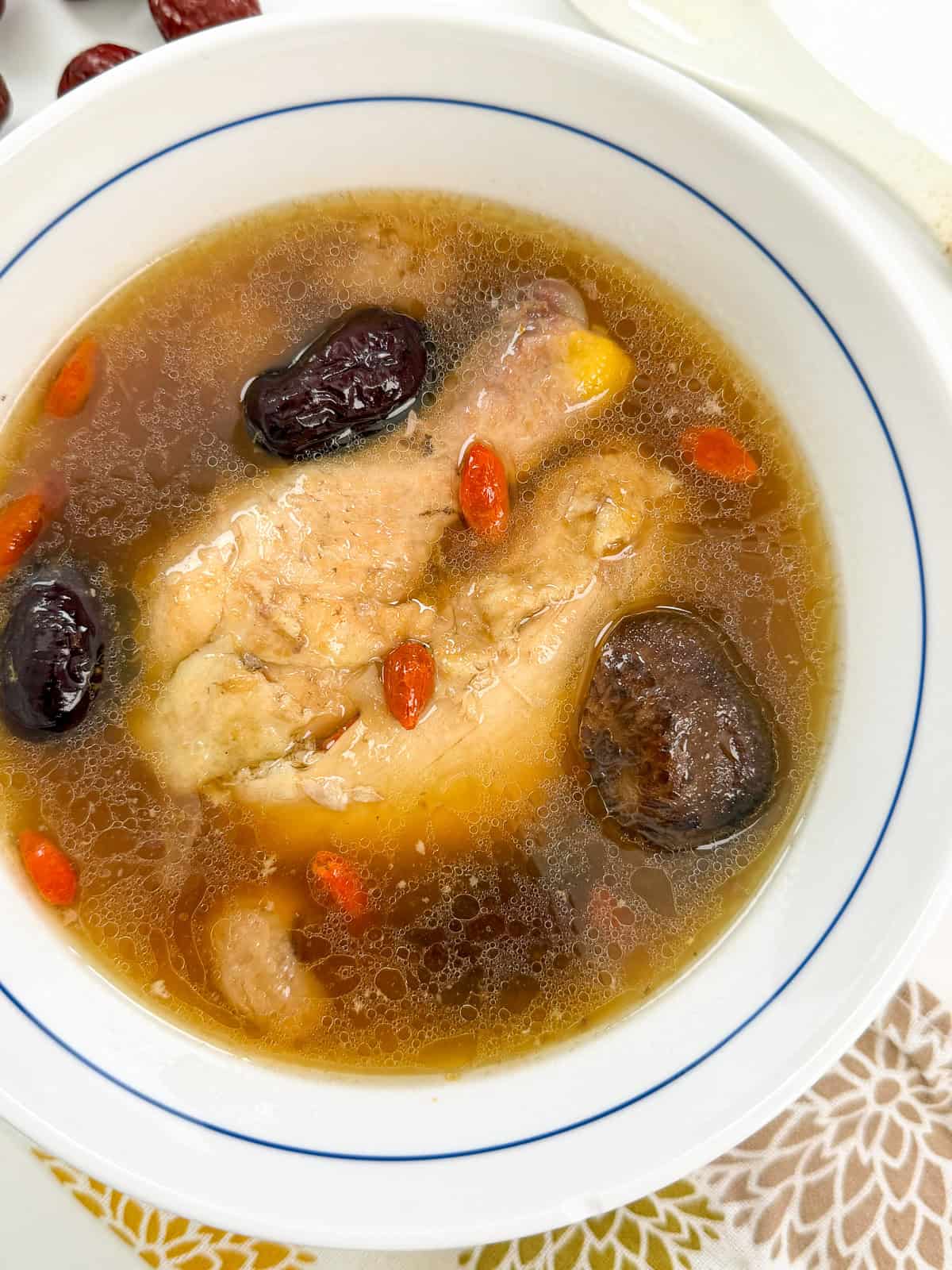 Chinese Chicken Herbal Soup in a white bowl with chicken thighs, shiitake mushrooms, goji berries