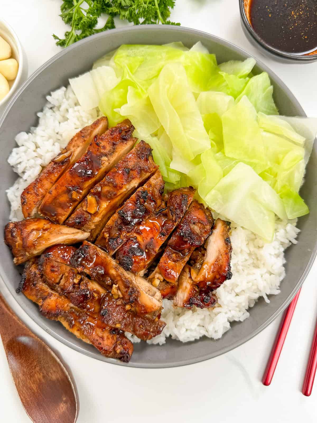 Five Spice Chicken in a bowl with white rice and cooked green cabbage. There is a brown spoon and red and gold chopsticks next to it.