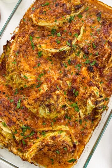 Marry Me Melting Cabbage in a large baking dish with a wooden spoon on the left and oven gloves to the right