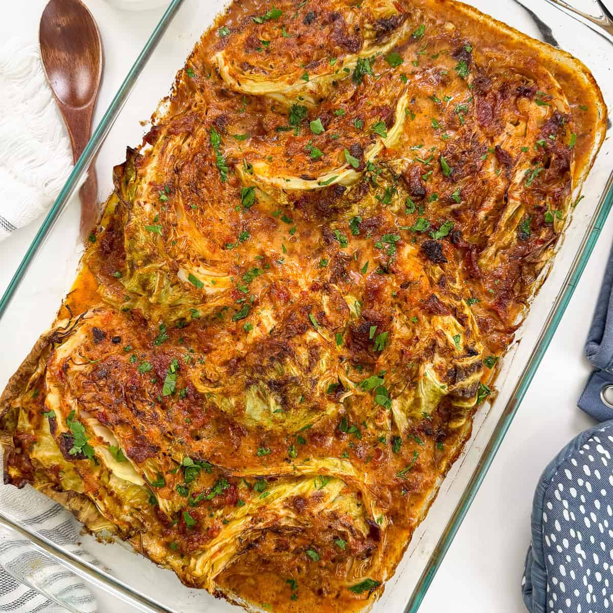 Marry Me Melting Cabbage in a large baking dish with a wooden spoon on the left and oven gloves to the right