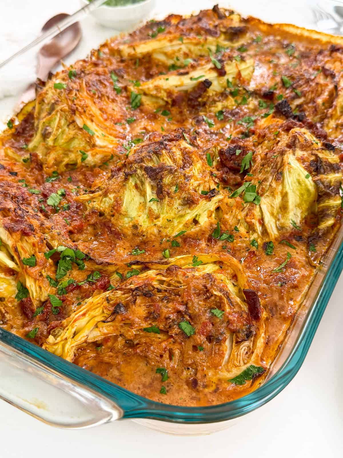 Marry Me Melting Cabbage in a large baking dish side view with a wooden spoon on the left