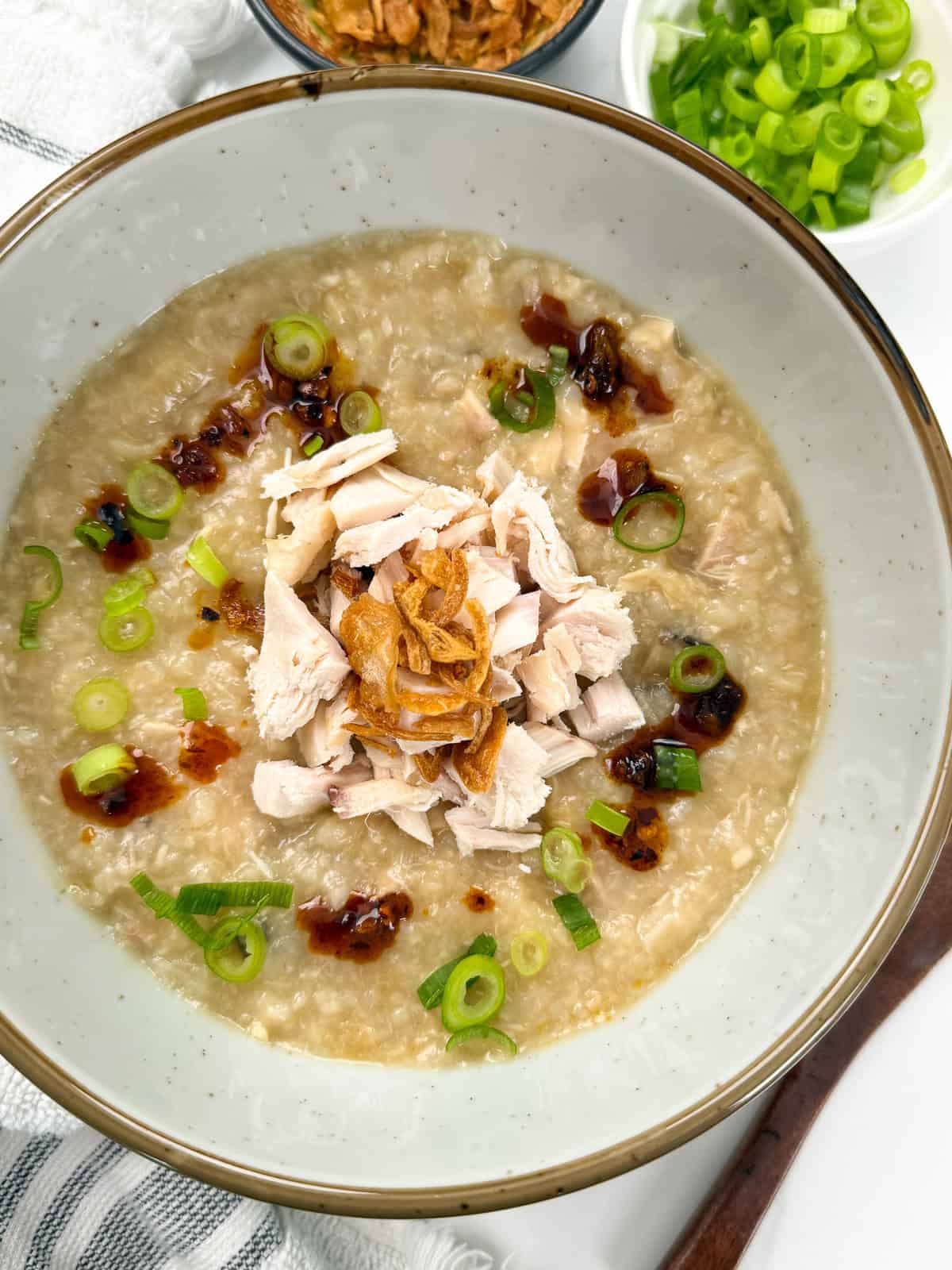 Rotisserie Chicken Congee with fried shallots and green onions on top. A wooden spoon is on the counter to the right.