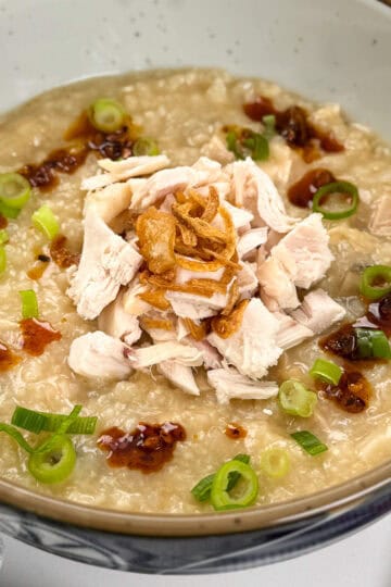 Rotisserie Chicken Congee zoomed in view with chopped chicken and fried shallots in the middle. A wooden spoon sits on the right side.