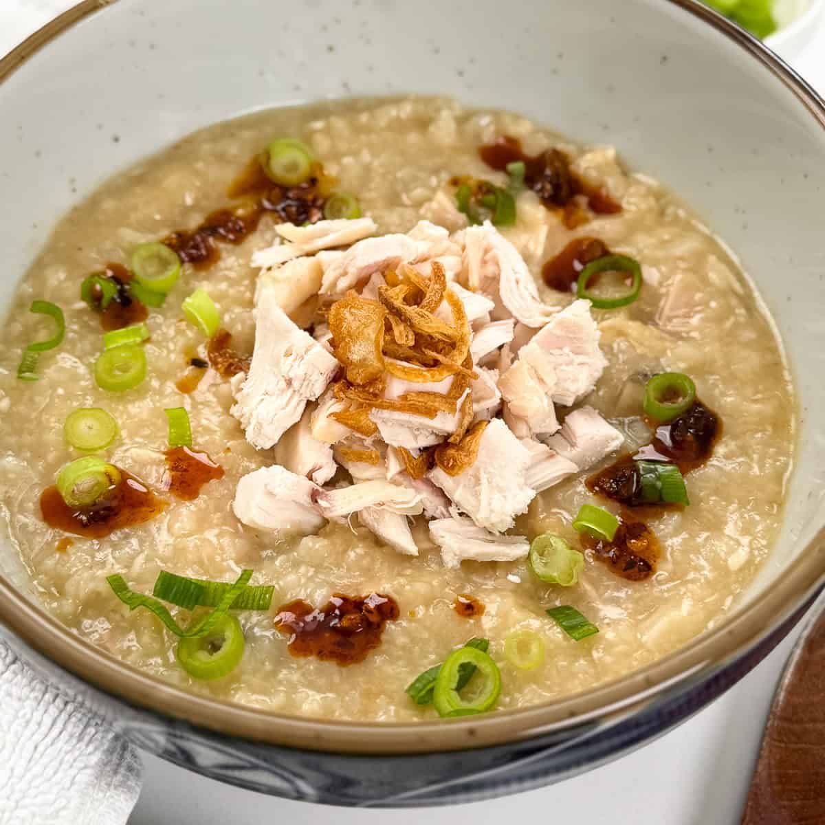 Rotisserie Chicken Congee zoomed in view with chopped chicken and fried shallots in the middle. A wooden spoon sits on the right side.