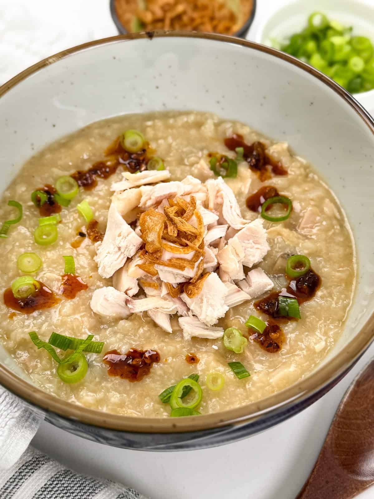 This is a side angle of Rotisserie Chicken Congee with fried shallots and green onions on top. A wooden spoon is on the counter to the right.