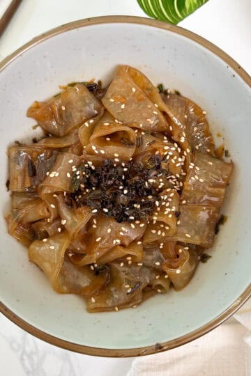 Scallion Oil Rice Paper Noodles in a bowl with chopsticks to the left and a plant at the top featured view