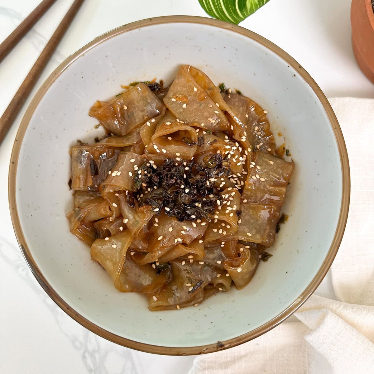 Scallion Oil Rice Paper Noodles in a bowl with chopsticks to the left and a plant at the top featured view