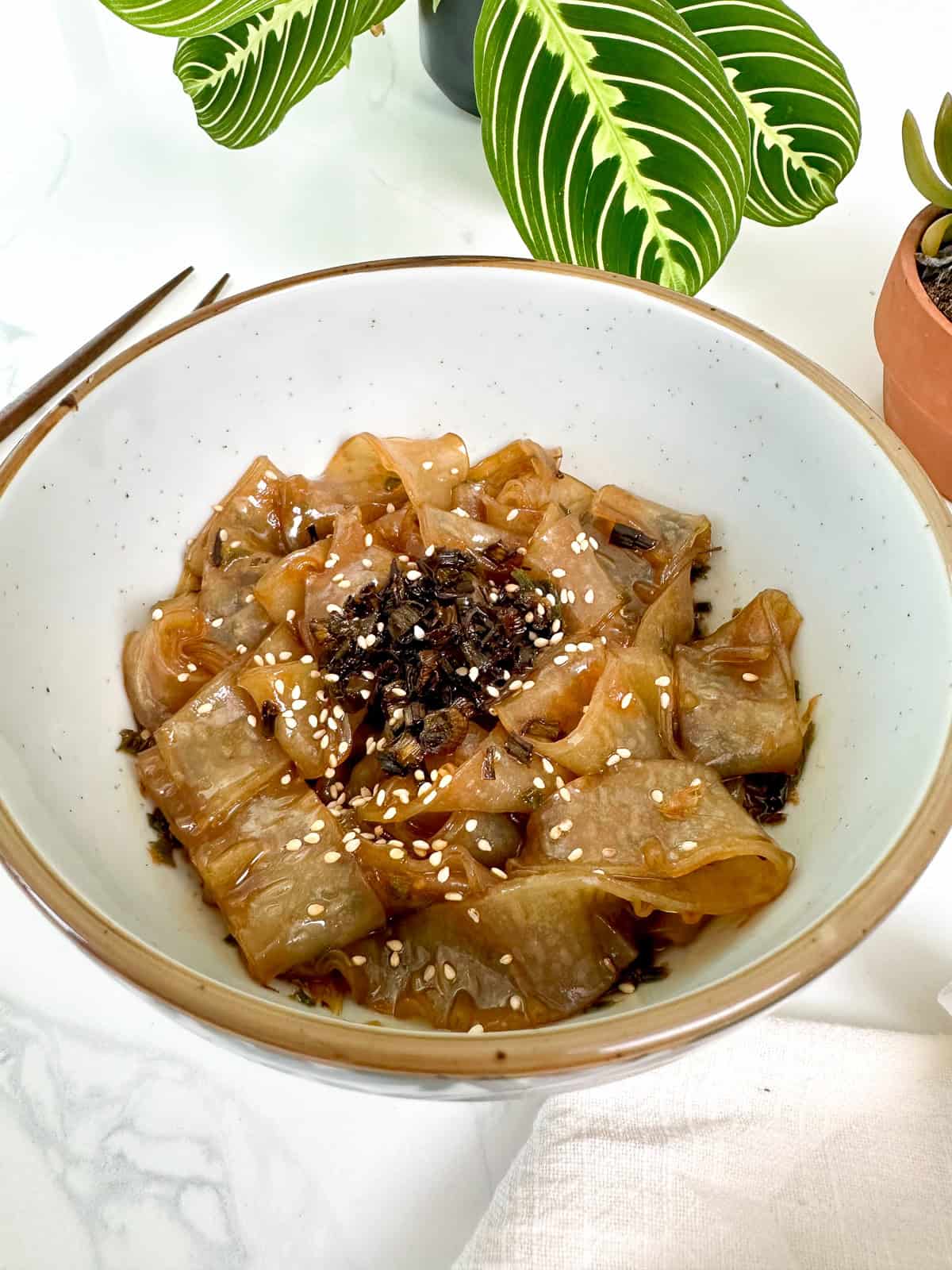 Scallion Oil Rice Paper Noodles in a bowl with chopsticks to the left from a side view