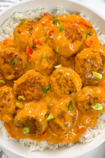 Thai Meatballs in a Red Curry Sauce sitting on top of a bed of white rice with green onions on top and a wooden spoon on the right
