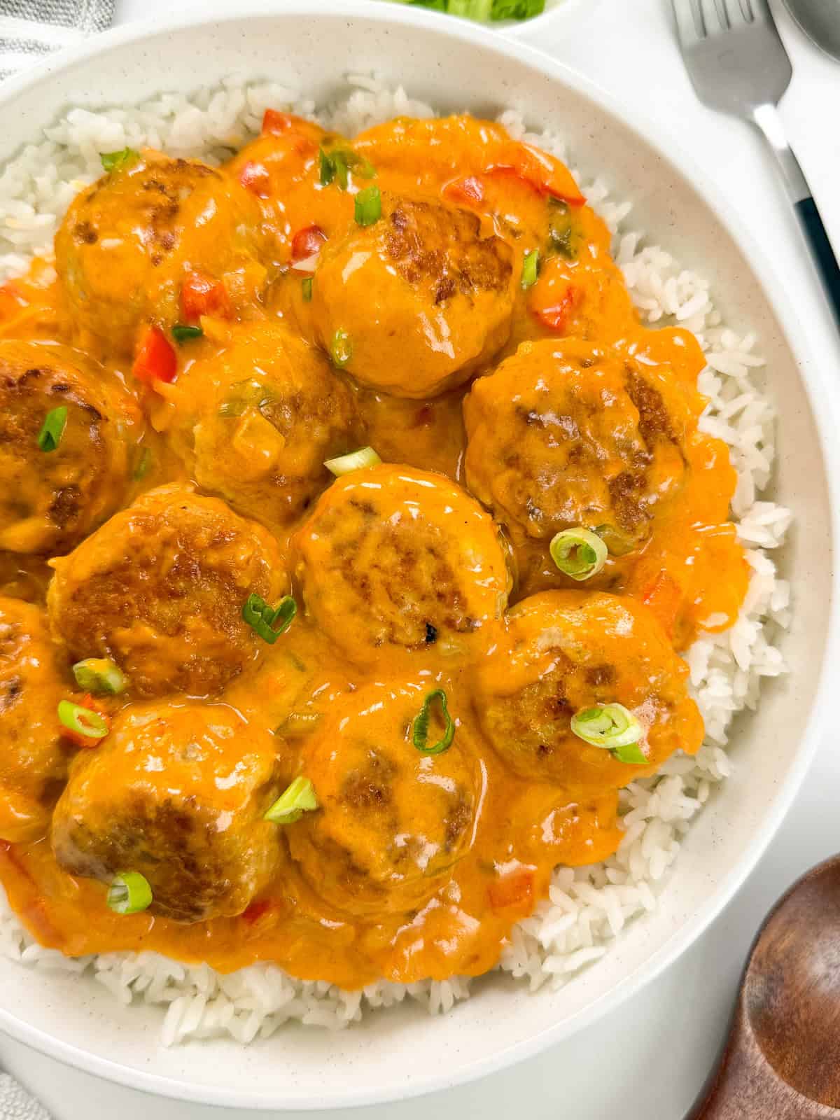 Thai Turkey Meatballs with Coconut Curry Sauce sit on top of a bed of white rice in a large bowl and a wooden spoon. The view is from top down.