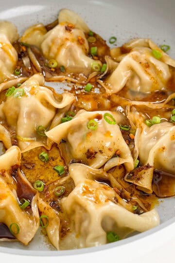 Viral Blanket Dumplings in a large skillet with chopped green onions, soy sauce, and chili oil