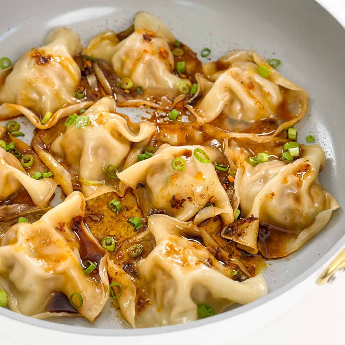 Viral Blanket Dumplings in a large skillet with chopped green onions, soy sauce, and chili oil