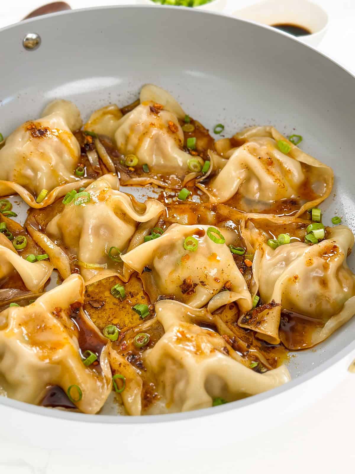 Viral Blanket Dumplings in a large skillet with chopped green onions, soy sauce, and chili oil