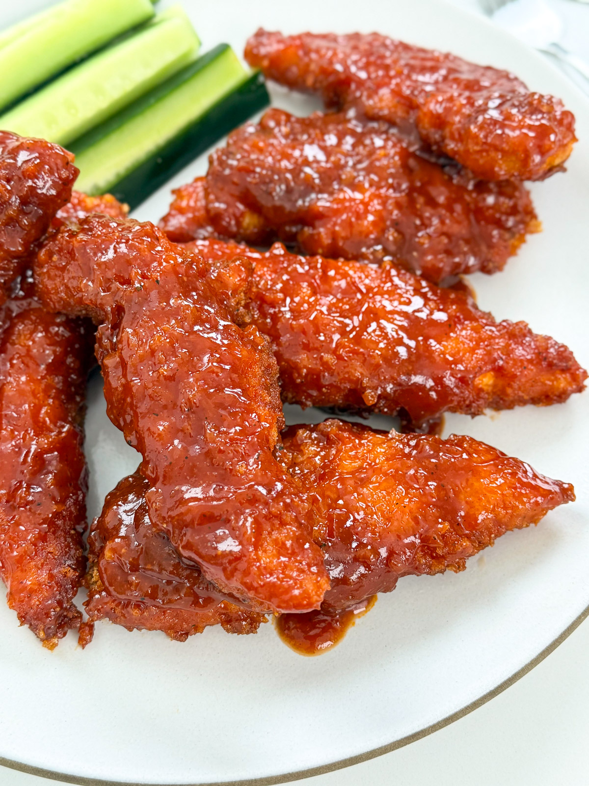 A plate of crispy Honey BBQ Chicken Tenders coated in a shiny, reddish-brown sauce, served with fresh cucumber sticks on the side.