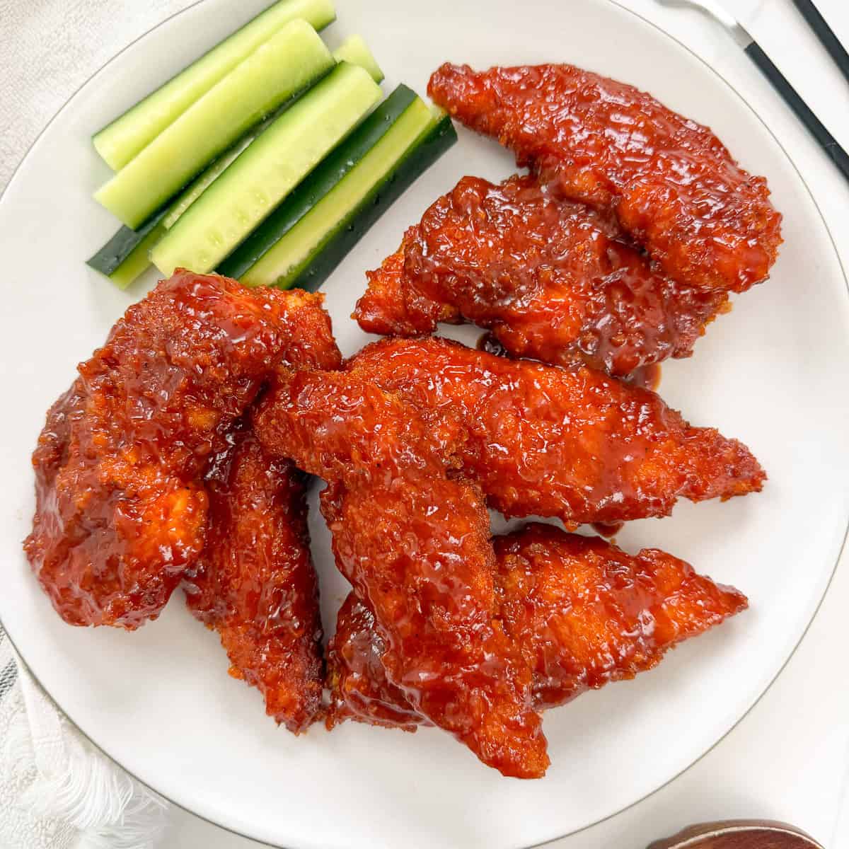 A white plate with several pieces of glazed Honey BBQ Chicken Tenders and a side of cucumber sticks.