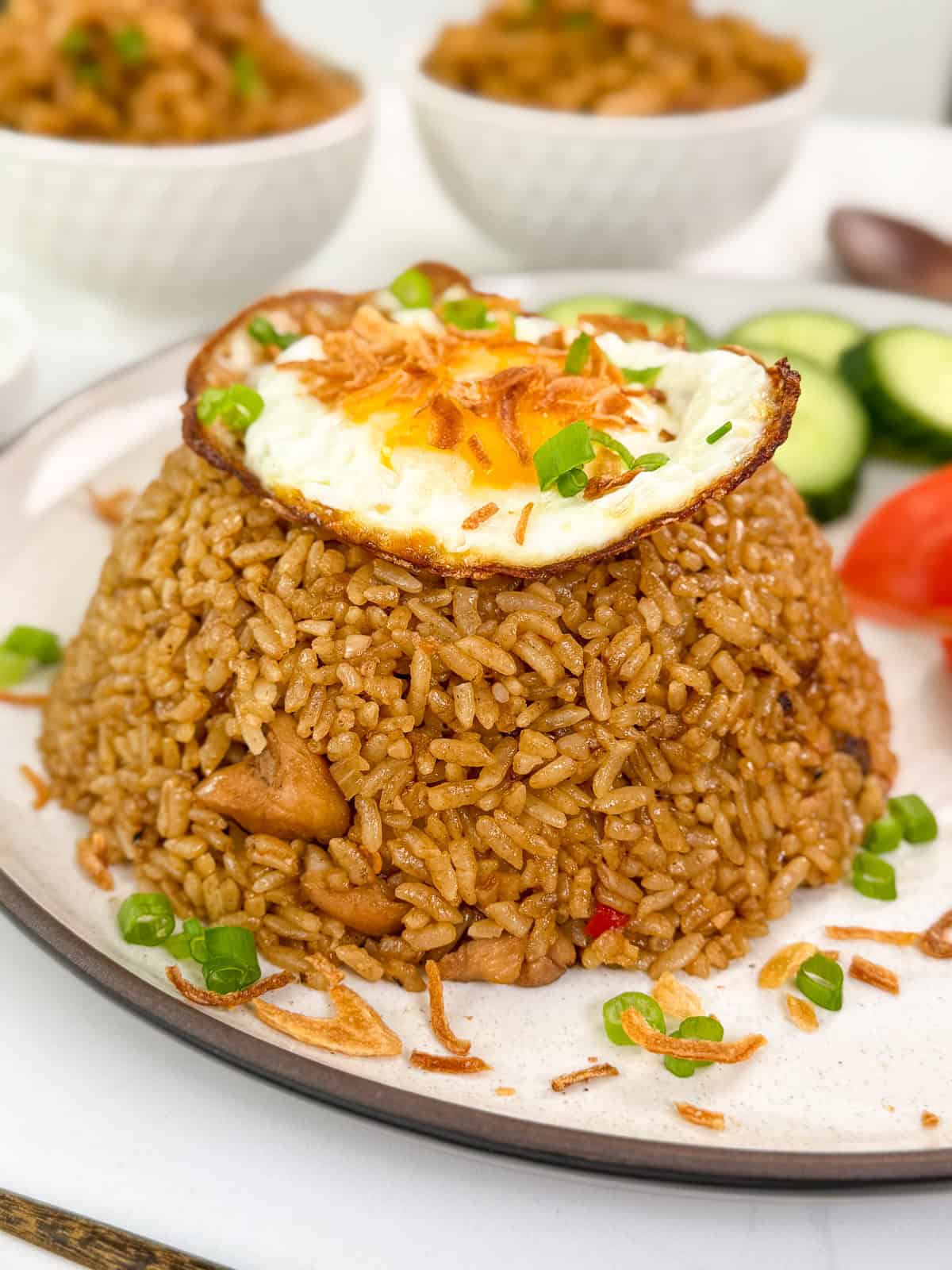 Nasi Goreng (Indonesian Fried Rice) on a plate with green onions, crispy fried shallots, and a fried egg on top.