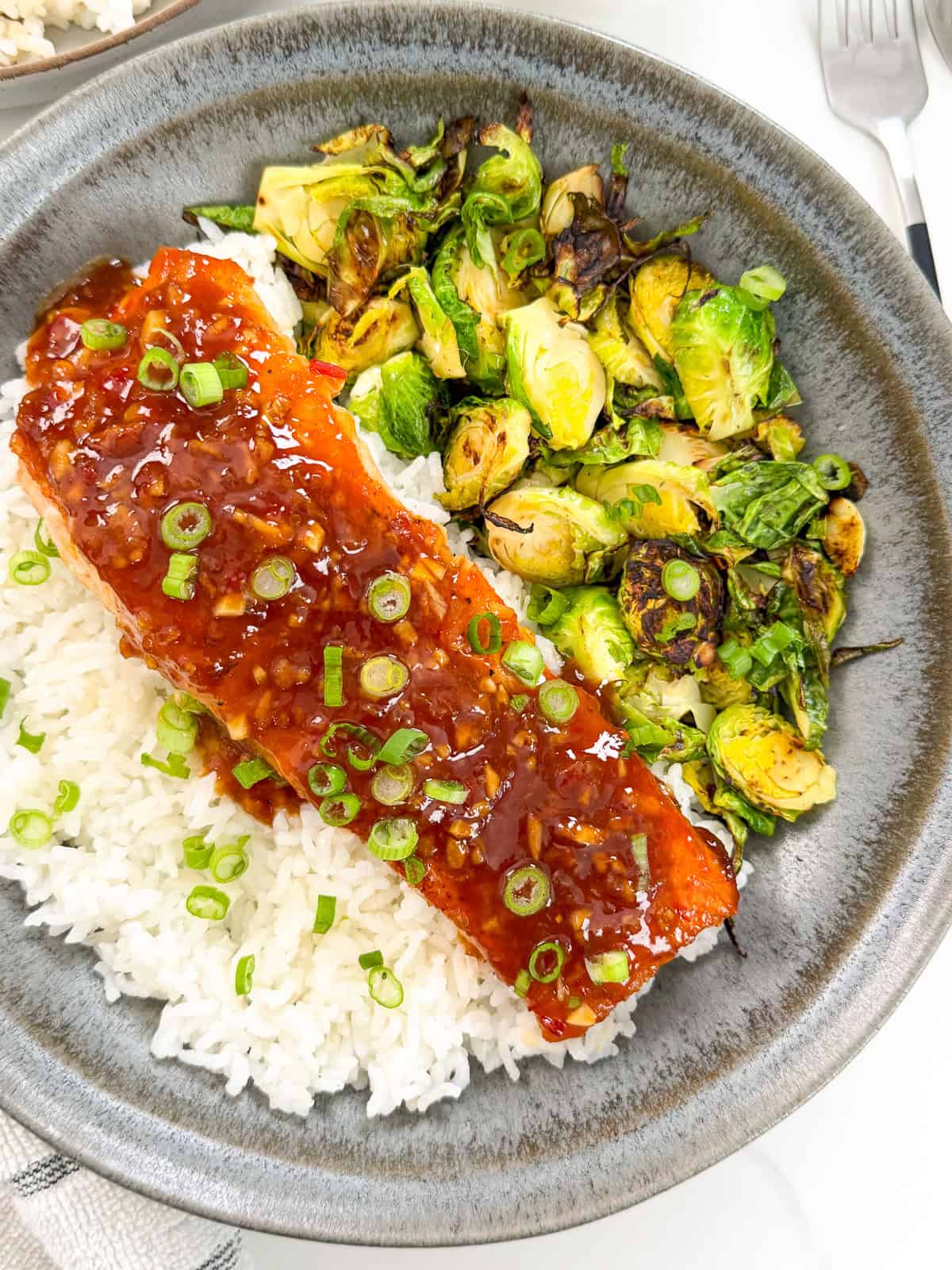 Sweet chili salmon on top of white rice with roasted brussels sprouts on the side top down view