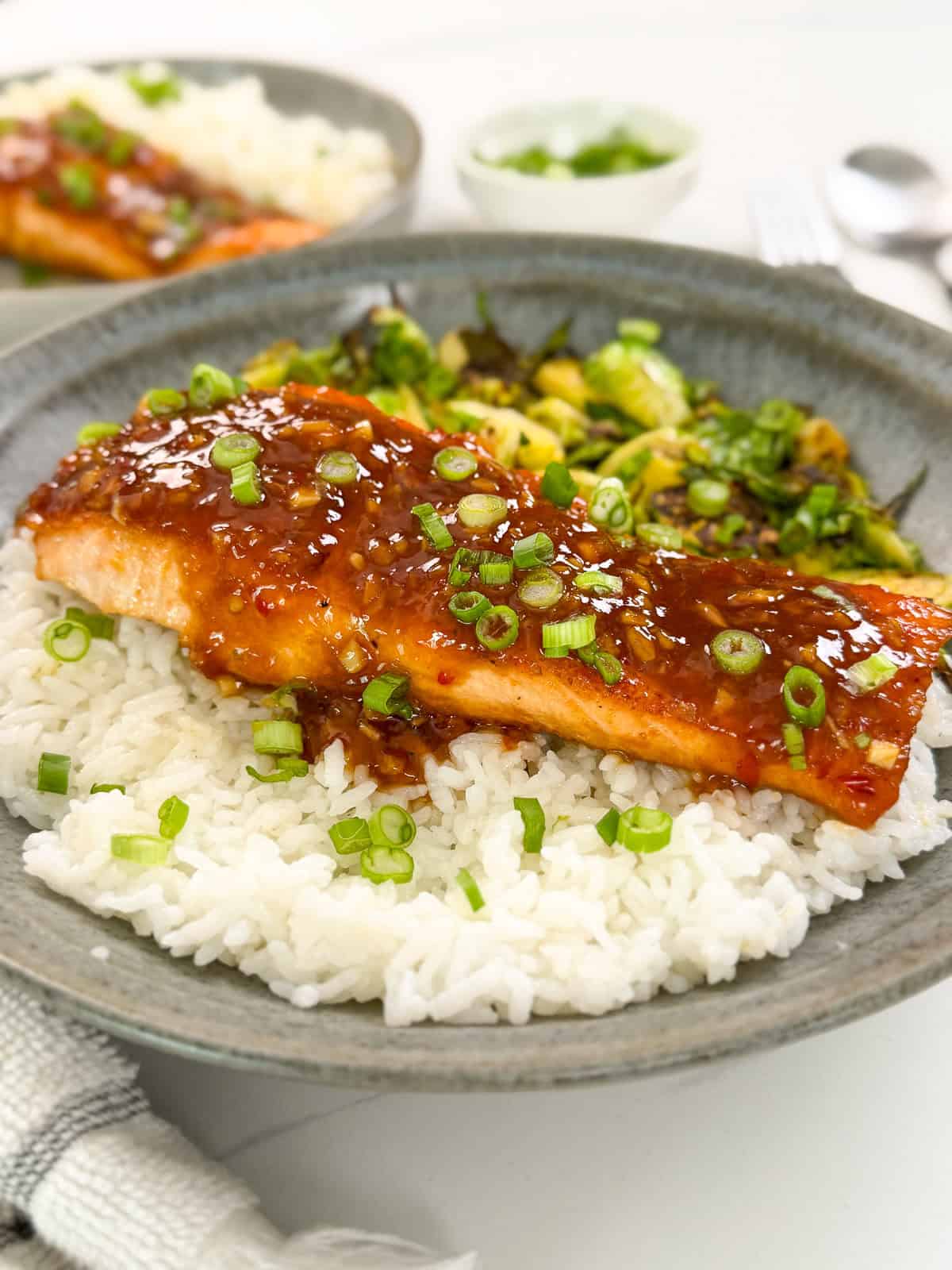 Sweet chili salmon on a bed of white rice with green onions on top and brussels sprouts to the side. This is a side view of the dish.