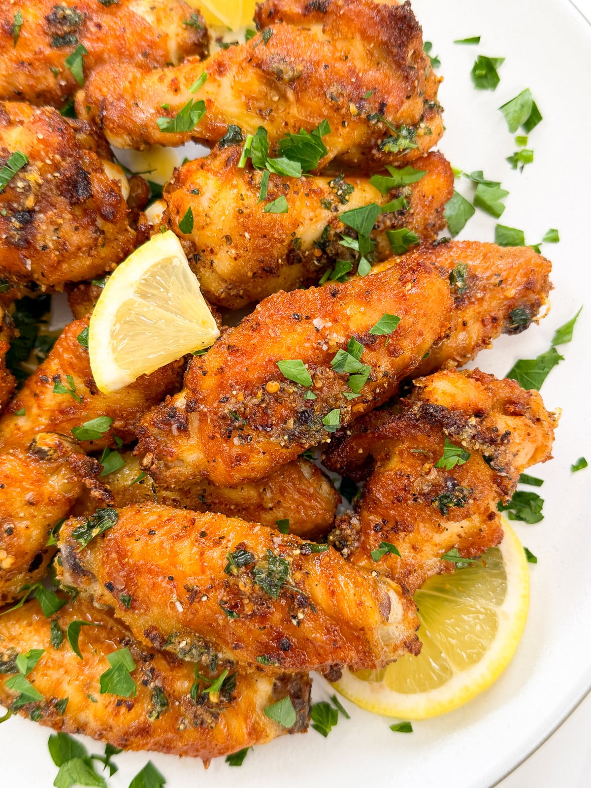 A plate of crispy, golden-brown Lemon Pepper Chicken Wings garnished with chopped fresh parsley and served with lemon wedges.