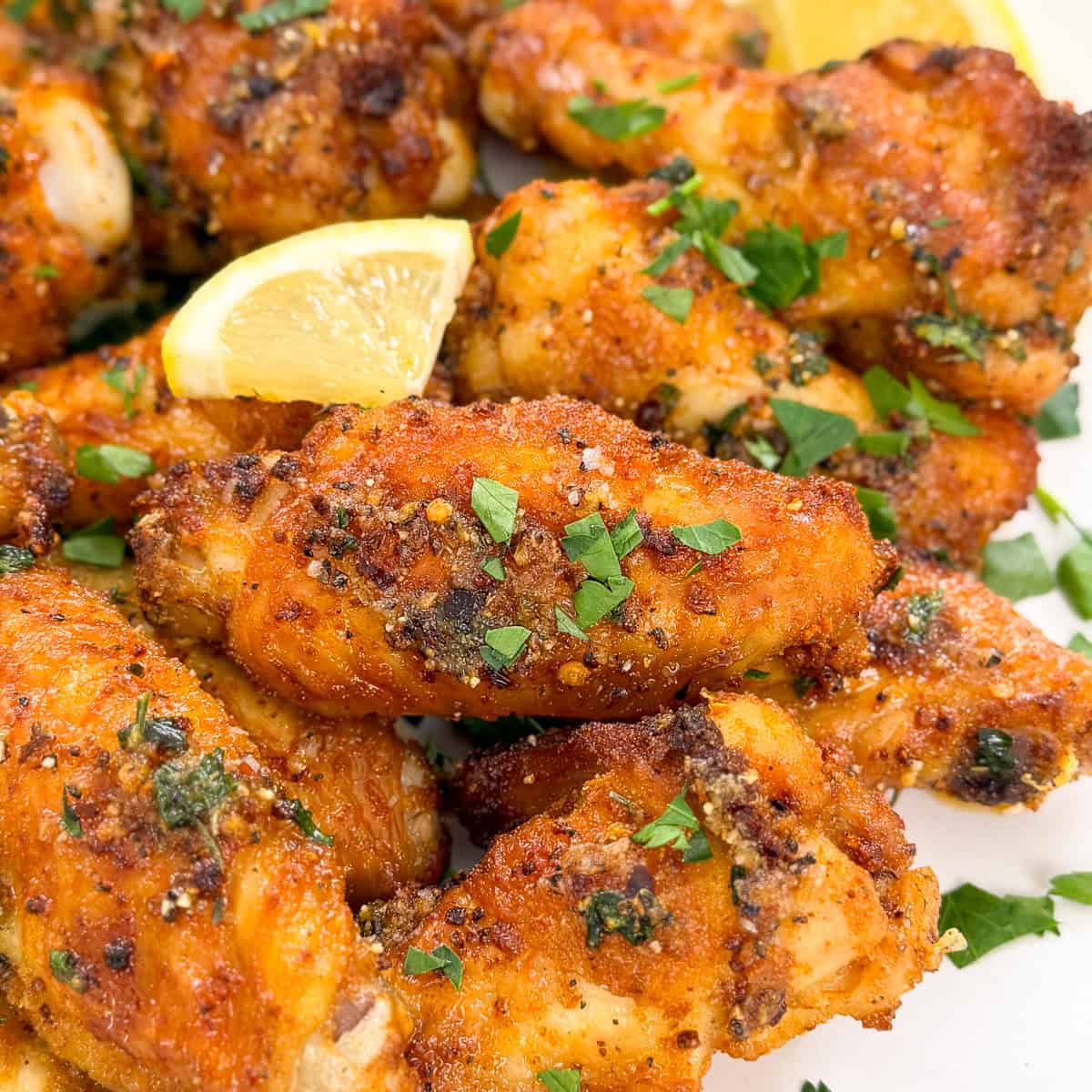 Close-up of crispy Lemon Pepper Chicken Wings, garnished with chopped parsley and lemon wedges. The golden brown wings look flavorful and perfectly seasoned, served on a white plate.