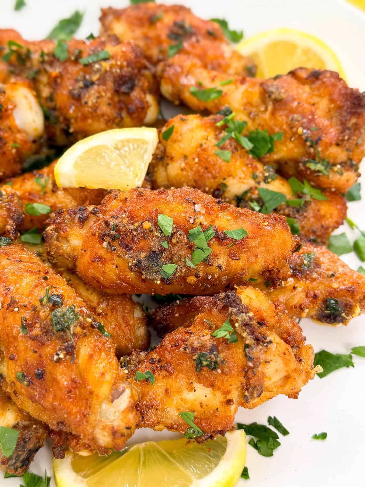 A plate of crispy Lemon Pepper Chicken Wings garnished with chopped parsley and lemon wedges, showcasing a golden-brown coating and fresh herbs.