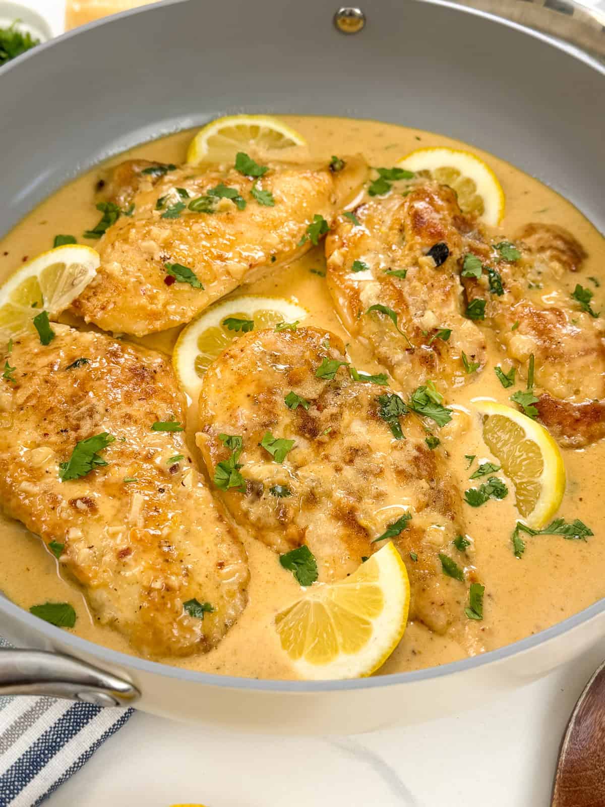 Creamy Lemon Garlic Chicken breasts in a luscious lemon sauce, garnished with fresh parsley and lemon slices in a gray skillet.