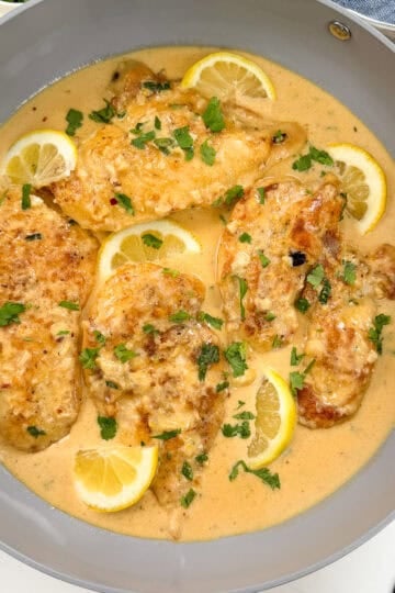 Creamy Lemon Garlic Chicken breasts in a velvety lemon sauce, garnished with chopped parsley and lemon slices, served in a gray skillet.