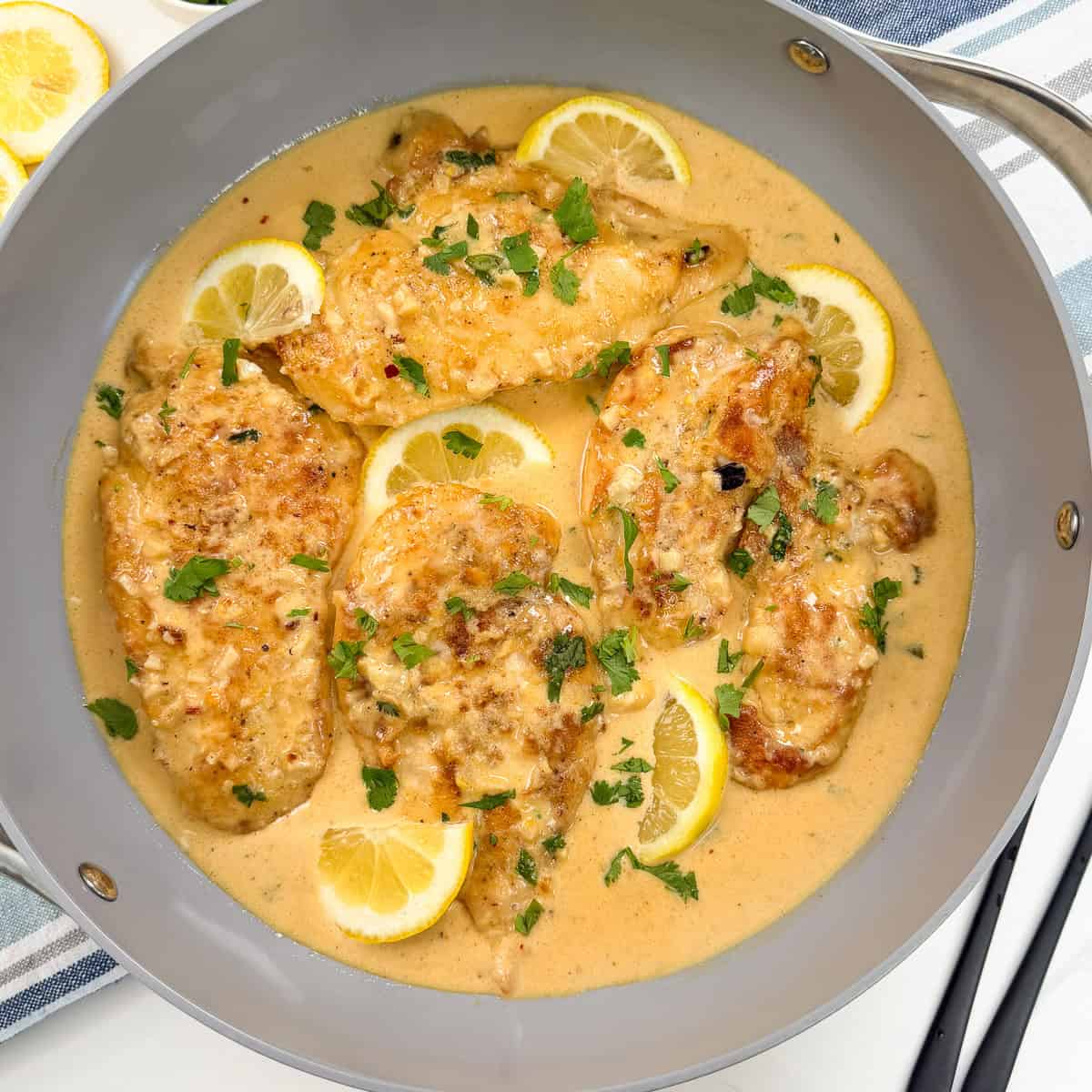 Creamy Lemon Garlic Chicken breasts in a velvety lemon sauce, garnished with chopped parsley and lemon slices, served in a gray skillet.