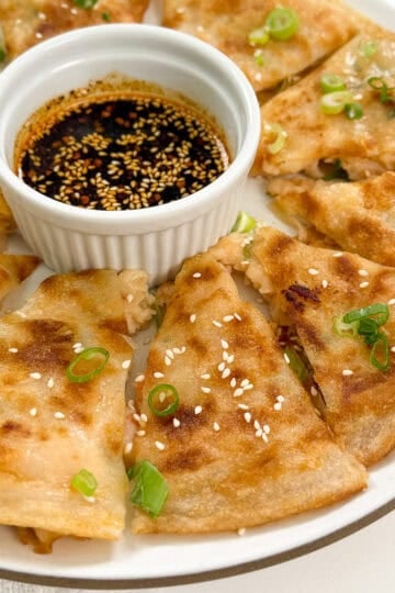 A plate of golden-brown, sliced Rice Paper Shrimp Pancakes arranged around a small dish of soy dipping sauce, garnished with sesame seeds and chopped green onions.