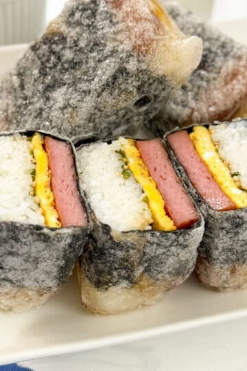 A plate of Teriyaki Spam Rice Paper Musubi, featuring layers of rice, egg, and pink meat wrapped in seaweed and crispy rice paper tempura batter on the outside.