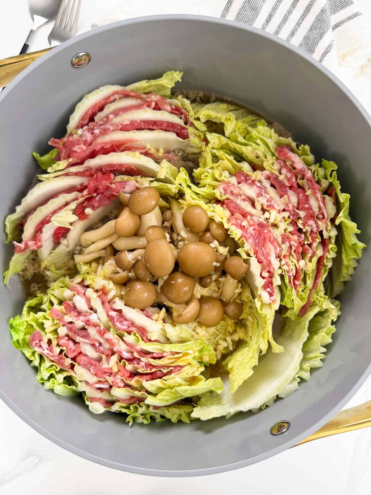 A pot filled with layered napa cabbage and thinly sliced beef arranged in a circle, with mushrooms and shimeji mushrooms placed in the center, ready to cook—this beautiful Mille-Feuille Nabe (Japanese Hot Pot) is a feast for both the eyes and the palate.