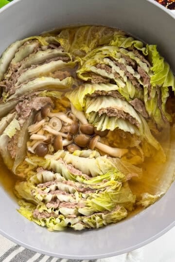 A pot filled with layers of cabbage and thinly sliced meat, cooked in broth, with mushrooms in the center—this delicious Mille-Feuille Nabe (Japanese Hot Pot) appears hot and ready to serve.
