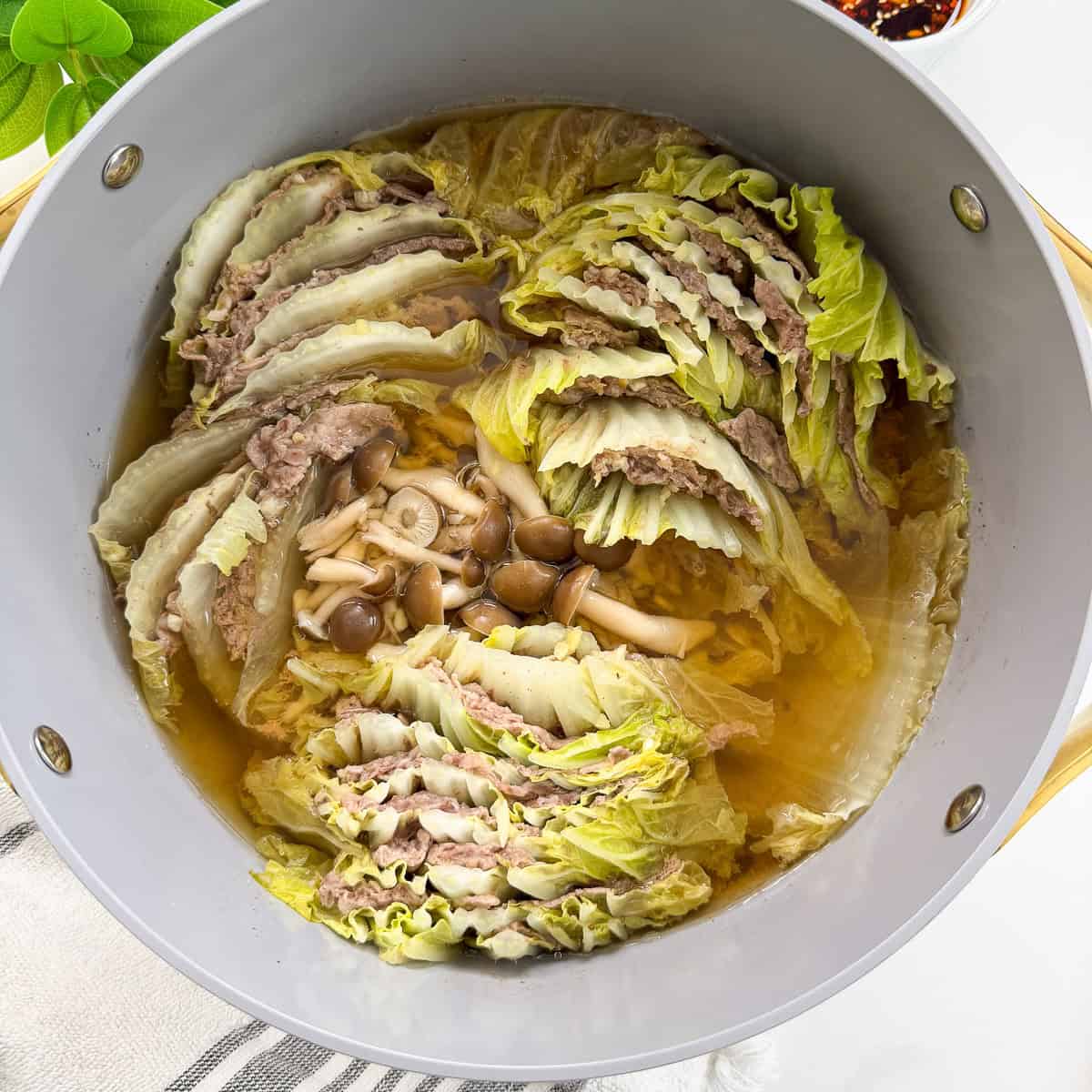 A pot filled with layers of cabbage and thinly sliced meat, cooked in broth, with mushrooms in the center—this delicious Mille-Feuille Nabe (Japanese Hot Pot) appears hot and ready to serve.