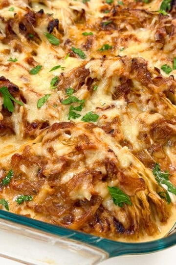 Baked French onion casserole topped with melted cheese and fresh parsley in a glass baking dish.