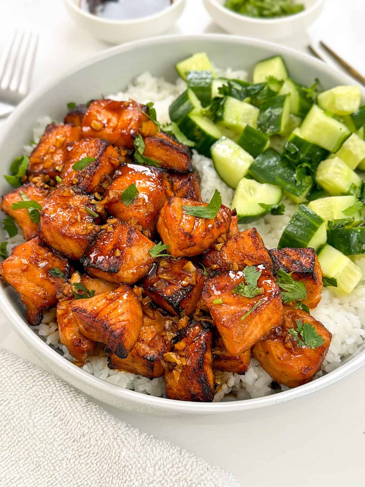 A bowl of glazed salmon bites and diced cucumbers served over white rice.