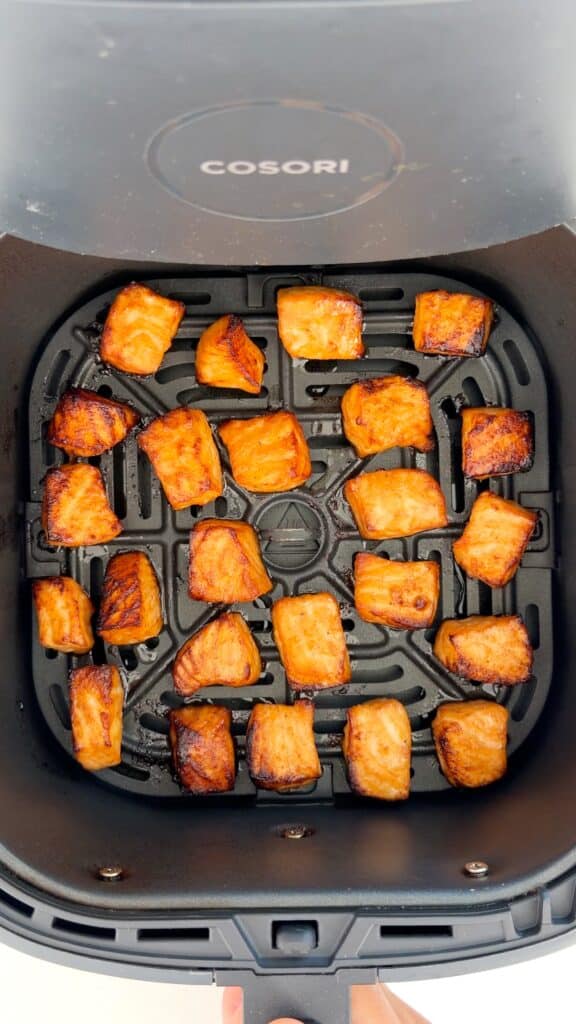 Golden-brown cubed pieces of cooked salmon inside the basket of a Cosori air fryer.